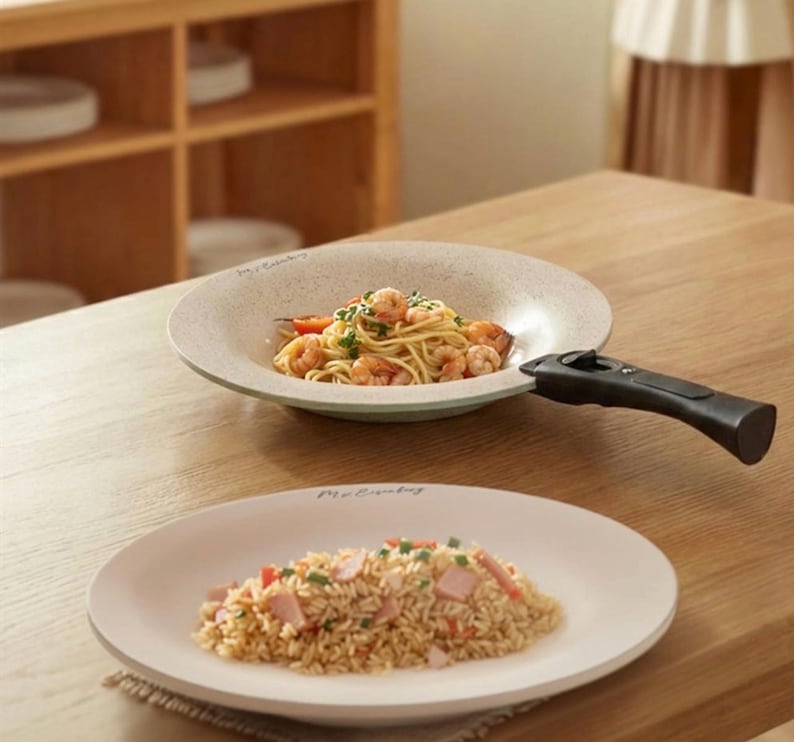 Puede incluir: Dos platos de cer&aacute;mica con comida sobre una mesa de madera. Uno contiene espaguetis con gambas y el otro arroz frito. El plato superior tiene un asa negra. Los platos son de color blanquecino con una textura moteada.