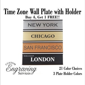 May include: Four time zone wall plates with holders. The plates are silver, gold, orange, and black. The plates are engraved with the city names: New York, Chicago, San Francisco, and London. The text "Buy 4, Get 1 FREE!!" is at the top of the image. The text "21 Color Choices" and "3 Plate Holder Colors" is at the bottom of the image.
