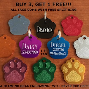 May include: Assortment of eight 1.3 inch paw print dog tags in various colors, including silver, red, black, purple, orange, pink, green, and gold. Each tag features a diamond-drag engraved design and includes a split ring. The tags are personalized with names and phone numbers, such as "Braxton", "Daisy", and "Diesel".