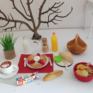 Peut inclure: Plusieurs miniatures de nourriture sur une surface blanche : une tasse de café, des pâtisseries aux framboises, une bouteille de jus, un panier et un panier rouge de produits de boulangerie. Une petite plante et une branche d'arbre décorative sont également présentes.