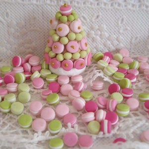 Può includere: Una torre di macarons rosa e verde con macarons sparsi intorno su un tovagliolo di pizzo bianco.