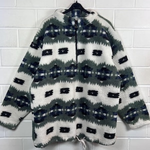 Könnte beinhalten: Ein langärmeliger Fleece-Pullover mit Stehkragen und kurzem Reißverschluss. Das Kleidungsstück ist mit einem strukturierten geometrischen Muster in Weiß, Salbeigrün und Dunkelmarineblau versehen. Am unteren Saum befindet sich ein Kordelzug.