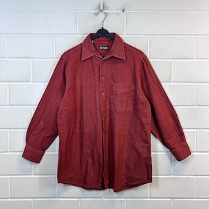 Può includere: Una camicia a maniche lunghe con bottoni di colore rosso scuro. La camicia ha una tasca sul petto e un colletto.