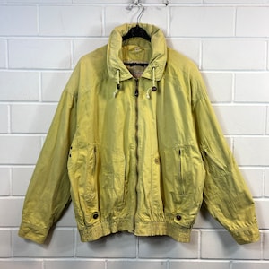 May include: A yellow lightweight jacket with a zipper closure, a hood, and elastic at the bottom. The jacket has two pockets on the front and a small pocket on the left sleeve.