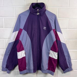 May include: A long-sleeve zip-up track jacket featuring a colour-blocked design in shades of purple, lavender, and white. The jacket has a high collar, elastic cuffs and hem, and a small white logo with the text "Leopard" on the upper chest.