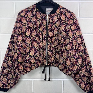 Peut inclure: Veste de style bomber noire ornée d'un motif cachemire rouge, jaune et doré. La veste est dotée d'une fermeture éclair, de poignets côtelés noirs et d'un ourlet à cordon. Le col est noir, et la veste est suspendue à un cintre noir.