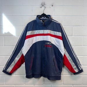 May include: A blue, red and white striped Adidas jacket with a silver stripe and the text "Team Adidas" on the front.