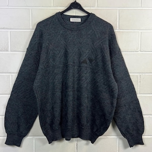 Könnte beinhalten: Dunkelgrauer Pullover mit Rundhalsausschnitt und langen Ärmeln. Der Pullover hat ein strukturiertes Muster und ein kleines Logo am Halsausschnitt. Gerippte Bündchen und Saum. Der Pullover hängt an einem schwarzen Kleiderbügel.