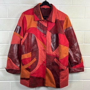 Könnte beinhalten: Eine Patchwork-Jacke in Rot-, Orange- und Burgundertönen. Die Jacke hat einen Kragen, eine Knopfleiste und Taschen. Das Design integriert verschiedene Texturen und Muster und schafft einen einzigartigen und künstlerischen Look.