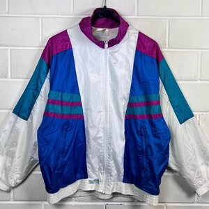 Pode incluir: Casaco vintage com blocos de cores branco, azul, verde-azulado e roxo. O casaco tem fecho de correr completo, gola alta e punhos e cós elásticos. O casaco está pendurado contra uma parede de tijolos brancos.