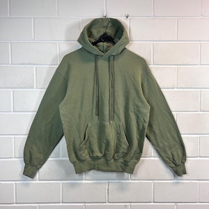 以下が含まれることがあります： カンガルーポケットとドローストリングフードが付いた緑色のフード付きスウェットシャツです。