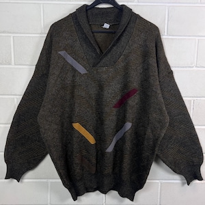 Può includere: Un maglione verde scuro con collo a scialle e accenti geometrici colorati. Il maglione presenta toppe grigie, gialle e bordeaux, che aggiungono un elemento di design unico alla maglieria.