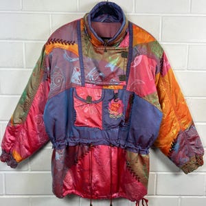 Könnte beinhalten: Bunte Vintage-Skijacke im Patchwork-Design. Die Jacke hat rote, orangefarbene, violette und grüne Paneele mit abstrakten Mustern. Sie hat einen hohen Kragen, mehrere Taschen und einen Kordelzug in der Taille. Der Text "DIVA" ist sichtbar.