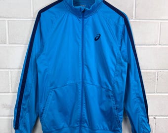 May include: A blue track jacket with a full-length zipper and a stand-up collar. The jacket features navy blue stripes down the sleeves and the Asics logo on the chest. The jacket is made of a smooth, lightweight material.
