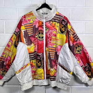 Könnte beinhalten: Eine bunte Vintage-Jacke mit einem geometrischen Muster in Rot-, Gelb-, Orange- und Weißtönen. Die Jacke hat einen Reißverschluss und einen weißen Kragen.
