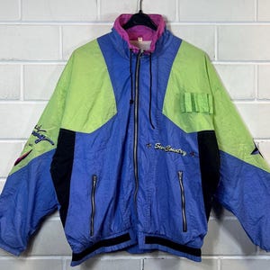 May include: A blue, green, pink and black windbreaker jacket with a zip fastening and the text "Sun Country" embroidered on the front.