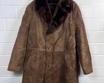 May include: A brown suede coat with a dark brown faux fur collar. The coat has a button-down front, two pockets, and a longline silhouette. The coat is hanging on a black hanger against a white brick wall.