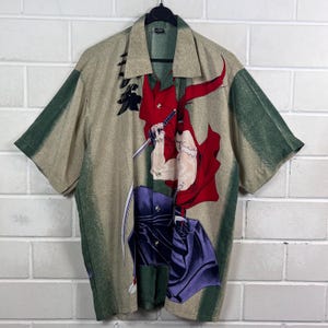K&ouml;nnte beinhalten: Beigefarbenes Button-up-Hemd mit einem gr&uuml;n-beigen Muster. Das Hemd zeigt eine Grafik eines Samurai-Kriegers in Rot und Lila, der ein Schwert h&auml;lt. Das Hemd hat kurze &Auml;rmel und einen klassischen Kragen.