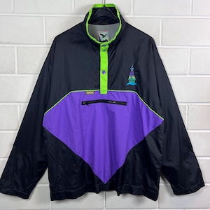 Op de afbeelding: Een zwart pullover windjack met een fel limoengroene kraag en sluiting met drukknopen. De voorzijde heeft een groot paars ruitvormig paneel, een zak met rits en een kleine geborduurde afbeelding van een toren. Het merklabel vermeldt Golfino.