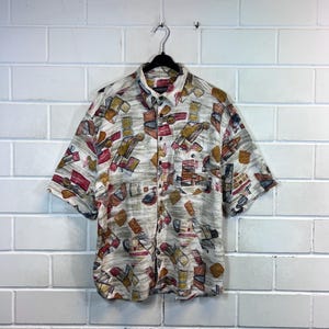 May include: A short-sleeved button-down shirt with a white background and a colorful geometric pattern. The shirt has a collar and a button closure.