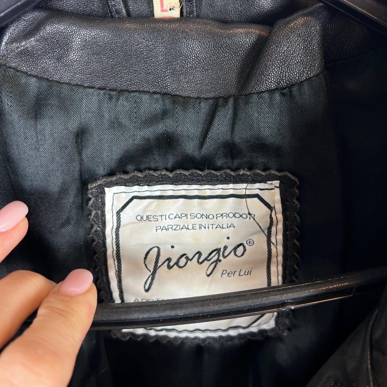 May include: Close-up of a black leather jacket's interior, showcasing a label with the brand name "Giorgio" and Italian text. The label is rectangular with a decorative border.