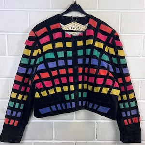 Könnte beinhalten: Eine schwarze Jacke mit einem Gittermuster aus rechteckigen Aufnähern in Rot, Pink, Gelb, Grün und Blau. Das Kleidungsstück hat einen Rundhalsausschnitt, lange Ärmel und eine Knopfleiste vorne. Das Etikett im Kragen zeigt den Text DINO'Z.