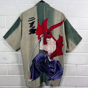 K&ouml;nnte beinhalten: Kurz&auml;rmeliges Hemd mit einer japanischen Anime-Illustration eines Samurai. Das Design zeigt einen Krieger in einem roten Umhang mit einem Schwert, vor einem beige-gr&uuml;nen Hintergrund. Das Hemd hat einen klassischen Kragen und kurze &Auml;rmel.