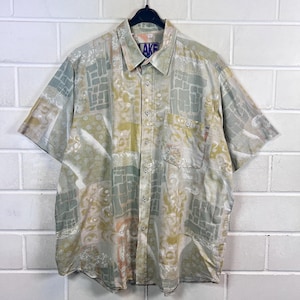 Op de afbeelding: Een kort mouw overhemd met knopen en een abstracte print in beige, bruin en groene tinten. Het overhemd heeft een knoopsluiting en een zak aan de linkerkant. Het label op het overhemd luidt "LAKE".