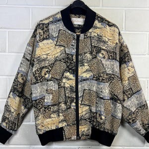 Puede incluir: Chaqueta bomber vintage con un diseño patchwork único. La chaqueta presenta un cuello, puños y dobladillo negros, con una cremallera de largo completo. El cuerpo principal de la chaqueta está estampado con una mezcla de estampado de leopardo e imágenes de mapas históricos en beige, negro y gris.