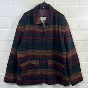 Könnte beinhalten: Vintage Wolljacke mit durchgehendem Reißverschluss und zwei Vordertaschen. Die Jacke hat ein farbenfrohes geometrisches Muster in Grün-, Burgunder-, Braun- und Marineblautönen. Der Kragen ist dunkelmarineblau.
