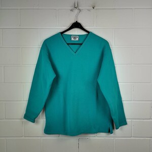 Könnte beinhalten: Ein türkisfarbener V-Ausschnitt-Pullover mit langen Ärmeln und einem kleinen weißen Etikett mit der Aufschrift "Washington State University".