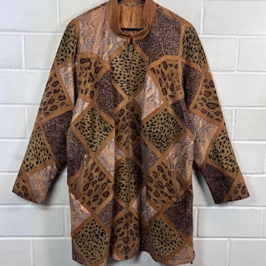 May include: A brown and tan jacket with a patchwork design. The jacket features a mix of animal print patterns, including leopard and snakeskin, arranged in a geometric pattern. It has a full zipper closure and two front pockets.