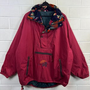 Könnte beinhalten: Burgunderfarbene Anorak-Jacke mit gemustertem Kragen und Viertelreißverschluss. Die Jacke hat zwei Reißverschlusstaschen und ein gesticktes Design in der Nähe der Taille. Der Kragen hat ein farbenfrohes geometrisches Muster. Die Jacke hängt an einem schwarzen Kleiderbügel.