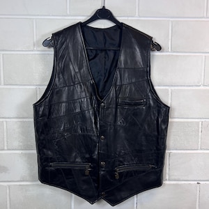 Könnte beinhalten: Eine schwarze Lederweste mit Patchwork-Design, V-Ausschnitt und Knopfleiste auf der Vorderseite. Das Kleidungsstück verfügt über zwei Reißverschlusstaschen an der Taille, eine kleine Brusttasche und ein glattes schwarzes Innenfutter.