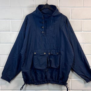 May include: A navy blue anorak jacket with a drawstring hood, a snap button closure, and a large kangaroo pocket. The jacket has a relaxed fit and a casual style.