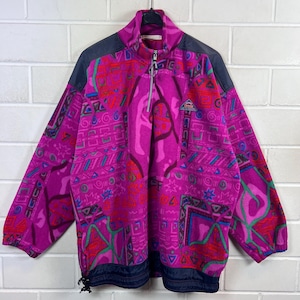 May include: A vibrant magenta fleece pullover featuring a high collar with a silver-toned half-zip closure. The garment displays a multi-coloured geometric pattern in shades of blue, green, and red, with dark navy panels on the shoulders and hem.
