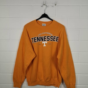 Könnte beinhalten: Oranges Sweatshirt mit Rundhalsausschnitt und dem Wort "TENNESSEE" in schwarzen Blockbuchstaben, das sich über einem weißen "T" -Logo wölbt. Das Wort "VOLUNTEERS" steht über dem Wort "TENNESSEE". Das Sweatshirt hat lange Ärmel und ein Lee-Markenetikett.