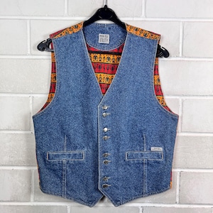 Peut inclure: Un gilet en jean bleu avec une doublure à motifs et le texte "HIS UTILITY". Le gilet a une fermeture boutonnée sur le devant, deux poches avant et une étiquette sur la poche avant. La doublure présente un motif géométrique rouge, orange et noir.