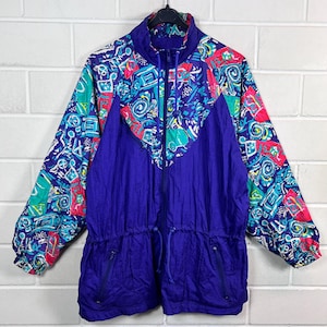 Pode incluir: Uma jaqueta roxa vintage com um padrão geométrico colorido nos ombros e na parte superior do peito. A jaqueta tem um zíper completo, uma cintura com cordão e dois bolsos frontais. As mangas são longas e com punhos.