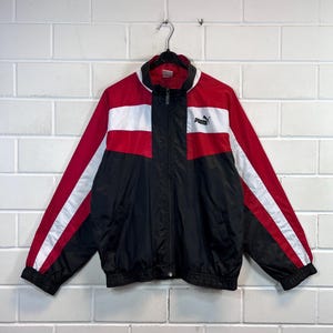 May include: A black, red and white windbreaker jacket with a zip fastening and the Puma logo on the chest.