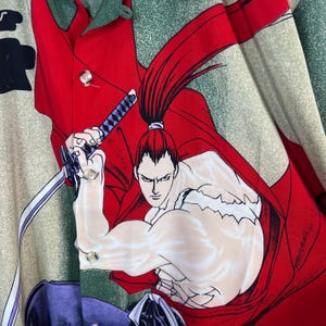 K&ouml;nnte beinhalten: Knopfleiste-Hemd mit einer lebendigen Illustration eines Samurai-Kriegers in Aktion. Das Design zeigt einen roten Umhang, ein Schwert und einen entschlossenen Ausdruck. Das Hemd hat einen gr&uuml;nen und beigen Hintergrund.