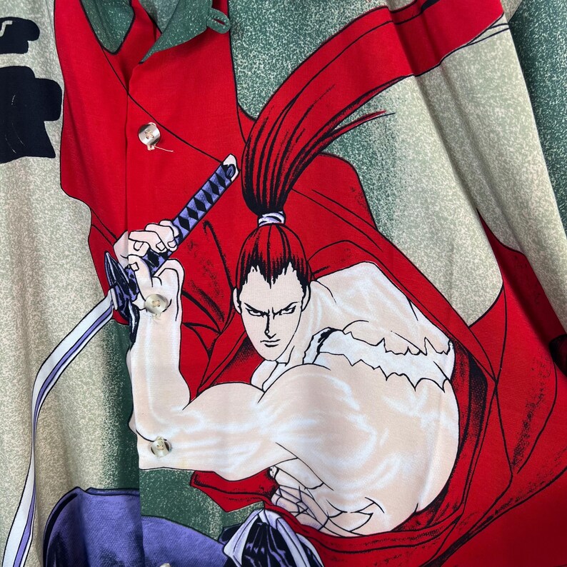 K&ouml;nnte beinhalten: Knopfleiste-Hemd mit einer lebendigen Illustration eines Samurai-Kriegers in Aktion. Das Design zeigt einen roten Umhang, ein Schwert und einen entschlossenen Ausdruck. Das Hemd hat einen gr&uuml;nen und beigen Hintergrund.