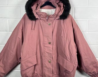 May include: A pink hooded jacket with a black faux fur trim around the hood. The jacket has a button closure and a drawstring at the waist.