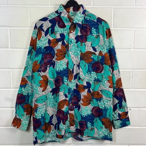 Könnte beinhalten: Ein langärmliges Hemd mit einem lebendigen Blumenmuster. Das Hemd hat einen grauen Hintergrund mit teal, orange und lila Blumendesigns. Es hat einen klassischen Kragen und geknöpfte Manschetten, perfekt für einen lässigen oder halbformellen Look.
