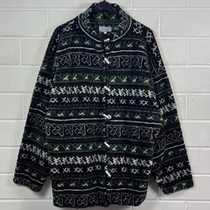 May include: A black and green patterned fleece jacket with a high collar and button closure. The jacket has a geometric design with white accents.