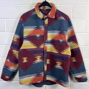 Op de afbeelding: Een overhemd met lange mouwen en knoopsluiting, voorzien van een veelkleurig geometrisch patroon in tinten blauw, bordeauxrood, oranje en geel. Het overhemd heeft een platte kraag, een knoopsluiting aan de voorzijde en mouwen met manchetten.