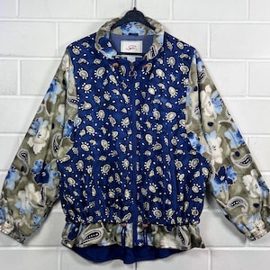 Könnte beinhalten: Eine blaue und grüne gemusterte Jacke mit Reißverschluss und Kordelzug in der Taille. Die Jacke hat ein Paisley-Muster und der Markenname "Silks" ist auf der Vorderseite aufgedruckt.