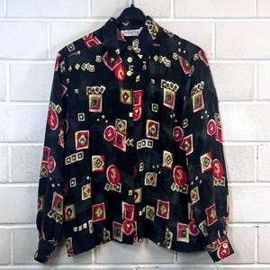 May include: Black patterned shirt with a button-down front. The design features red, yellow, and green geometric shapes on a black backdrop. The shirt has long sleeves and a collared neckline.