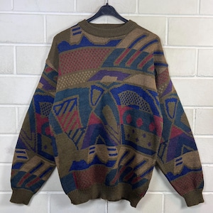 Könnte beinhalten: Ein langärmeliger Strickpullover mit einem mehrfarbigen geometrischen Muster in Braun-, Blau-, Rot- und Violetttönen. Das Kleidungsstück hat einen Rundhalsausschnitt, gerippte Bündchen und einen gerippten Saum mit einem komplexen Webmuster.