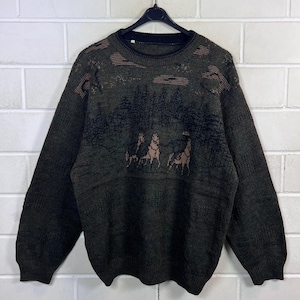 Può includere: Un maglione a maniche lunghe verde oliva scuro con una grafica lavorata a maglia nera raffigurante un paesaggio boschivo con tre cavalli in primo piano. Il capo a girocollo presenta colletto, polsini e orlo a coste, con una trama testurizzata.